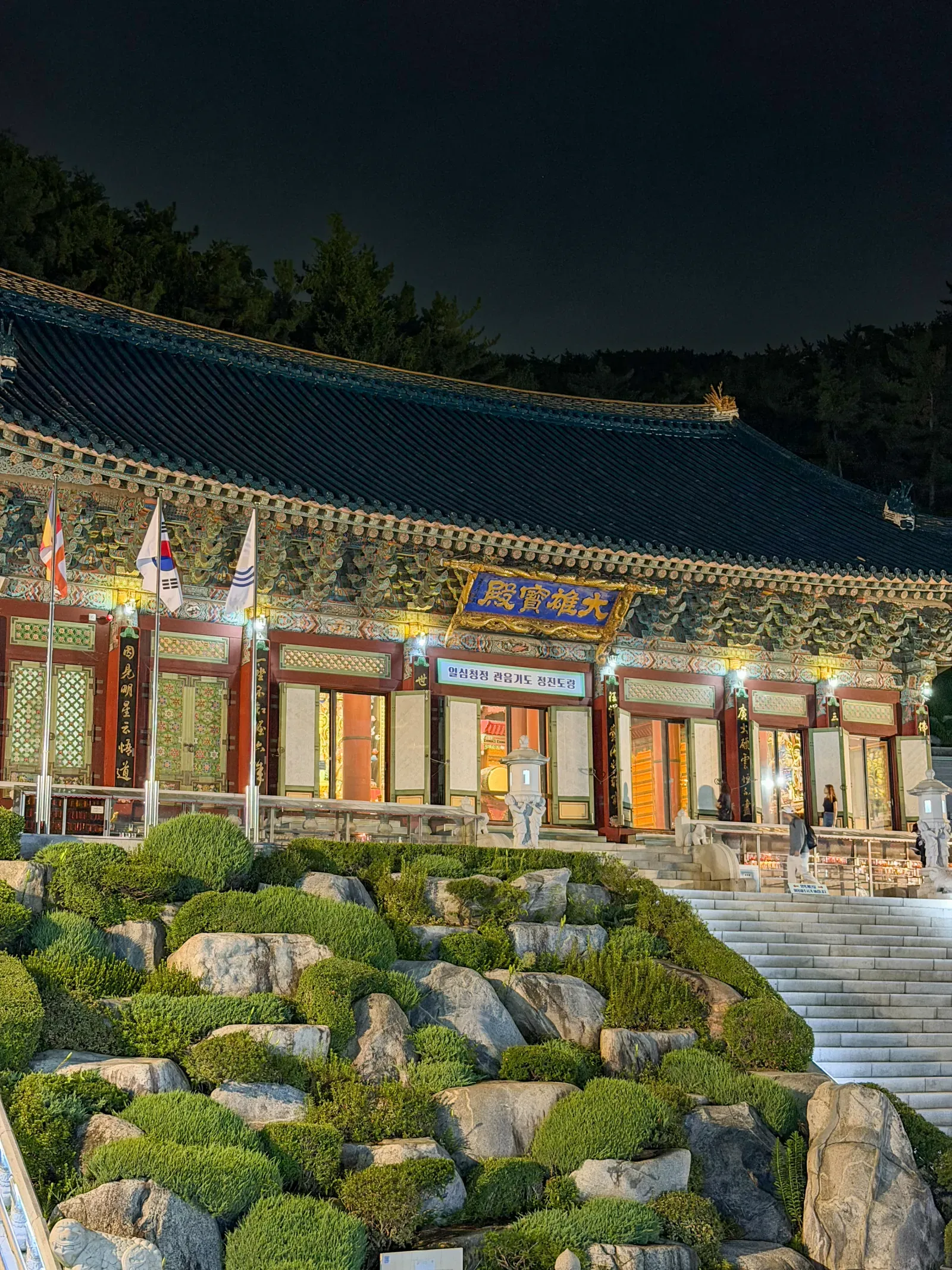 A temple at dusk in Busan, lit, with a formal garden and stone