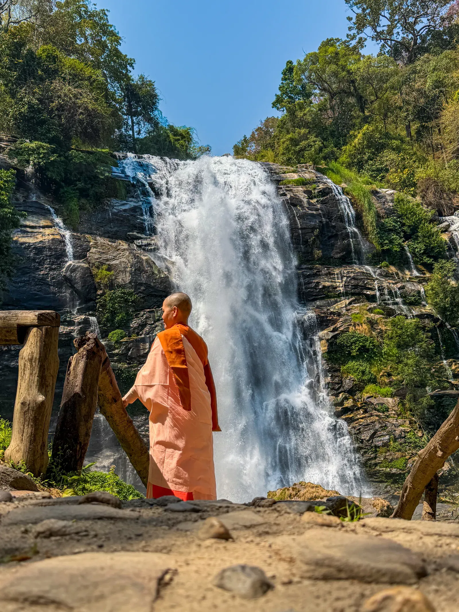 A figure in orange robes beside a tall waterfall near Chiang Mai