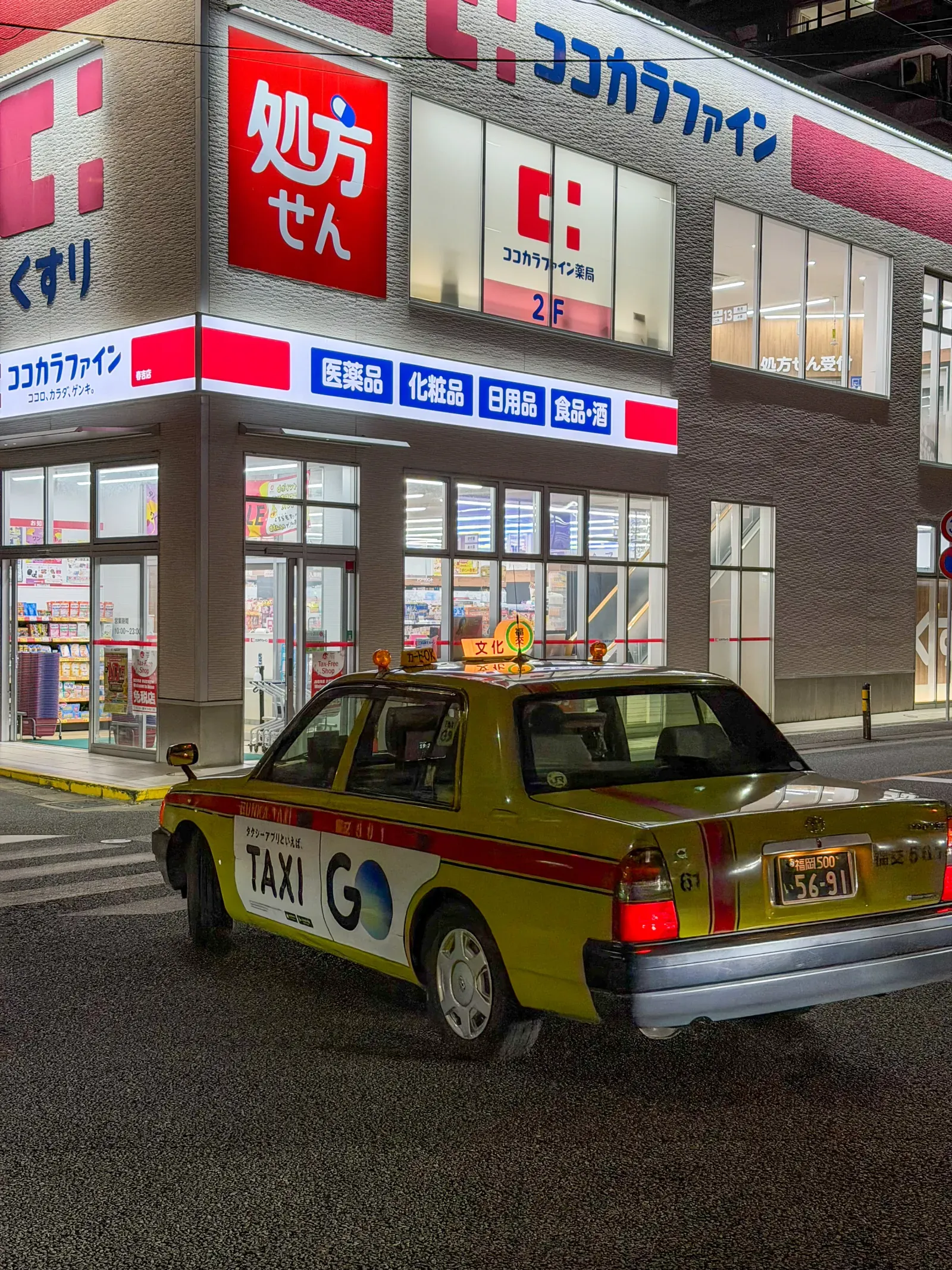 A lit shopfront and a taxi on a Fukuoka street at night
