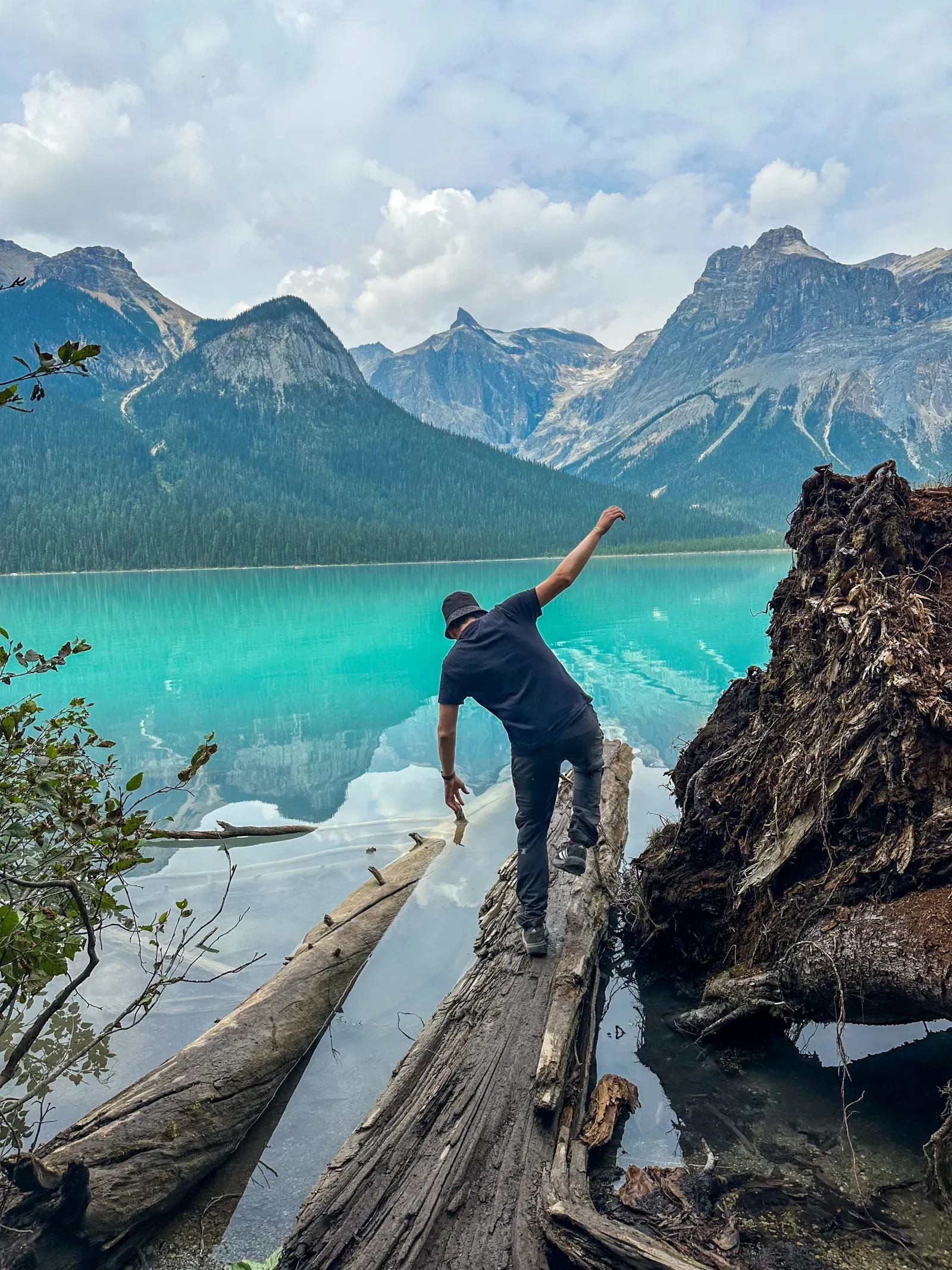 A person sitting on a fallen log at a turquoise glacial lake, mountains behind