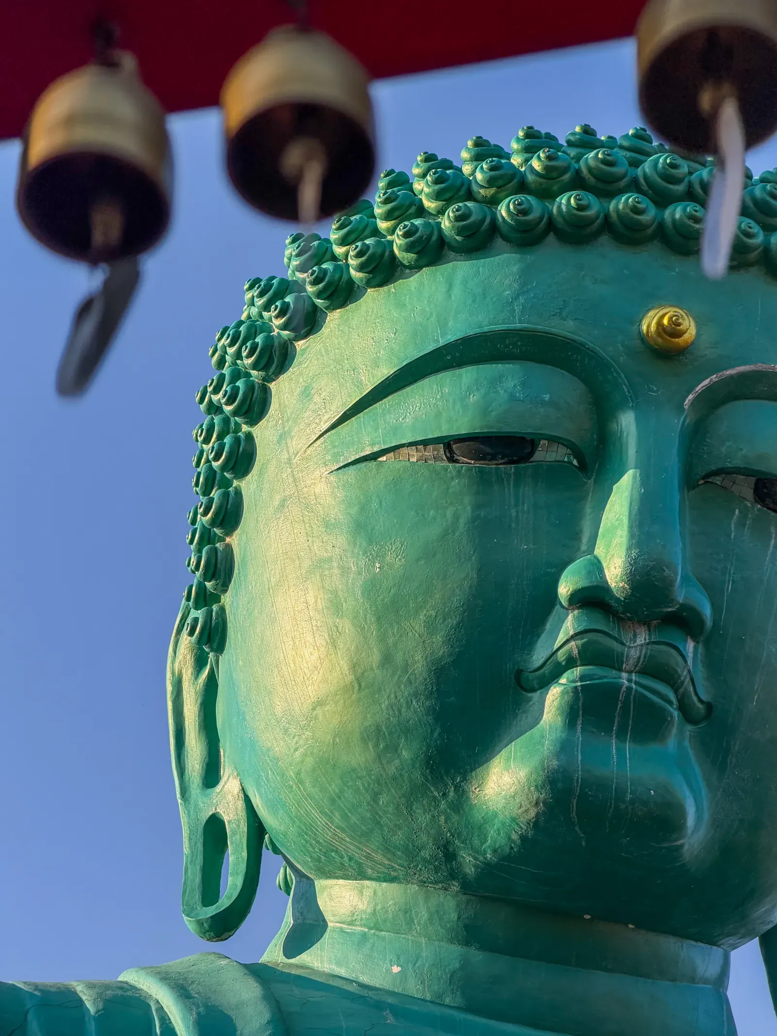 A bronze Buddha head, close, against the sky