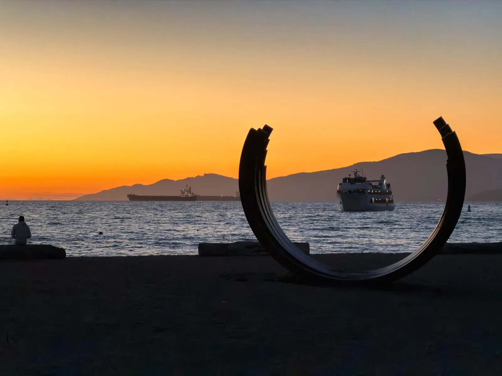Sunset over the water in Vancouver: a dark sculptural arch, ships on the water